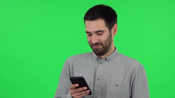 Portrait of Brunette Guy Is Texting on His Phone and Smiling. Green Screen
