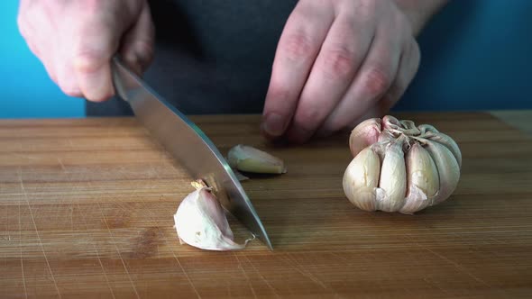 Peeling and Slicing Fresh Garlic on a Wooden Chopping Board in the Kitchen