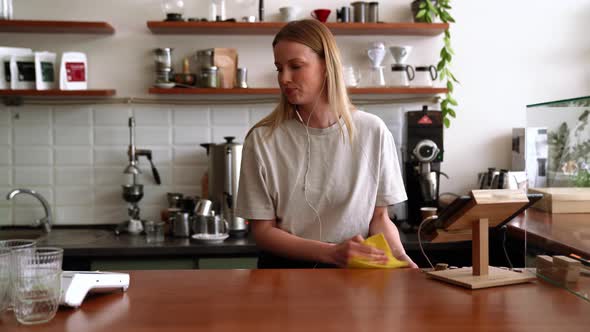 Laughing blonde woman barista wipes the table