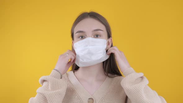 Girl Takes Off a Medical Mask on a Yellow Background