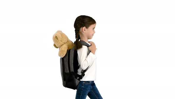 Cute Little Girl Walking To School with a Teddy Bear Sticking Out of Her Backpack on White