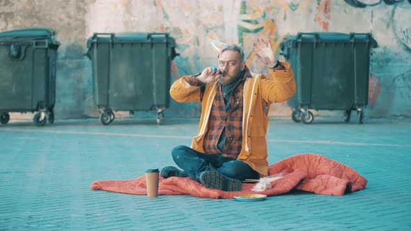 A Tramp is Sitting on the Ground and Cheering in a Birthday Hat