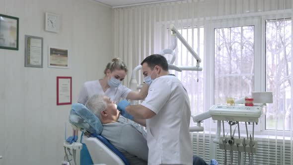 Dentist with Assistant in Protective Masks Working with Patient in Dental Clinic