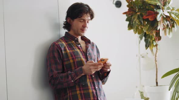 Cheerful adult man in a plaid shirt texting by phone and talking