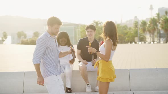 Multiethnic Friends Dancing with Drink Bottles in Hands Under Warm Evening Sunshine Outdoors