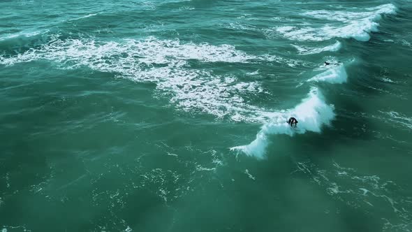 A drone shot of a surfer catching a small wave, surfing towards the shoreline.