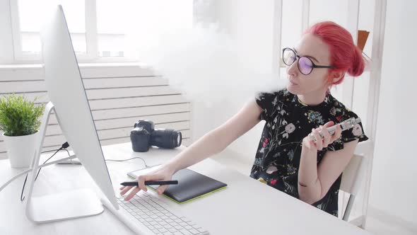 Photo Editor with Colored Hair Works Used Graphics Tablet at a Computer and Smokes Vape