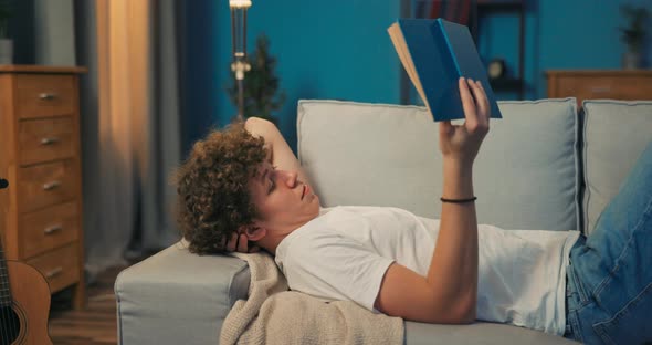 A Young Boy with Dark Curly Hair Lies on a Couch in the Living Room alt
