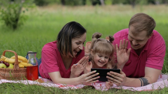 Family Weekend Picnic. Daughter Child Girl with Mother and Father Watching Online Movies on Tablet