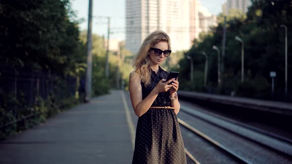 Woman Using Mobile Phone And Waiting Public Transport On Train Station. Active Lifestyle On Vacation