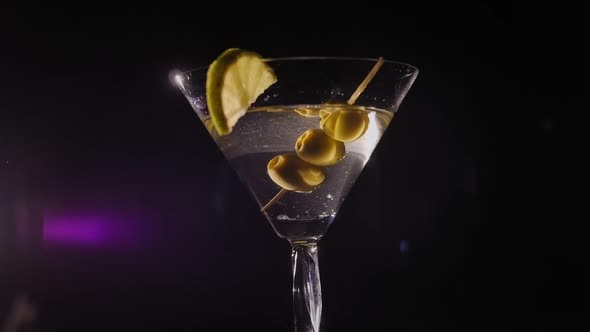 Closeup of a Martini Glass with Olives and Lemon Rotating on a Black Background