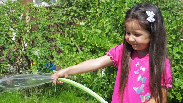 Little Cute Girl Holds a Watering Hose in Her Hands