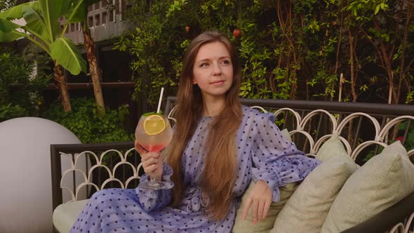 Happy Woman Holding Glass with Orange Cocktail While Sitting on Couch