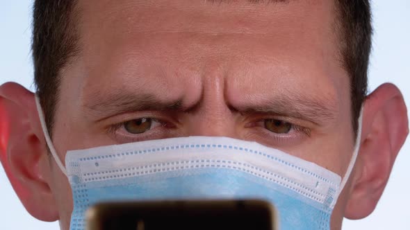 Man in Protective Face Mask Looks at Smartphone Holding It in Hands on Street