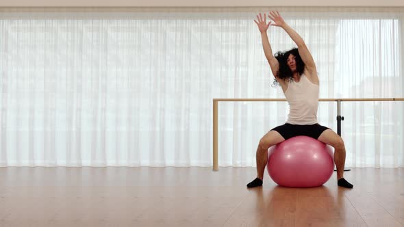 Muscular Guy with Long Wig Stretches on Pink Exercise Ball