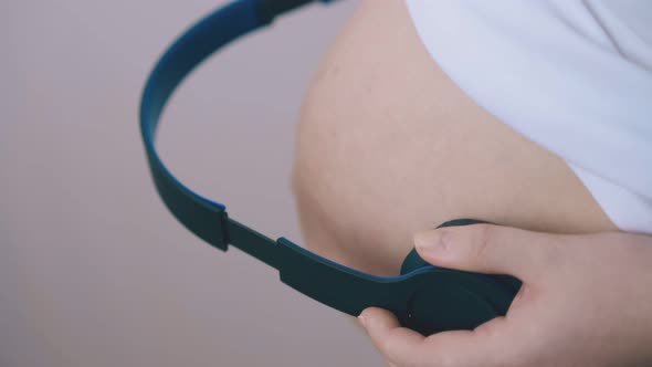 Pregnant Woman Puts Headphones to Tummy in Room Closeup