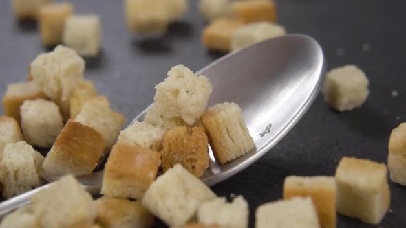 Fresh toasted bread wheat croutons fall into a teaspoon on a kitchen slate surface in slow motion