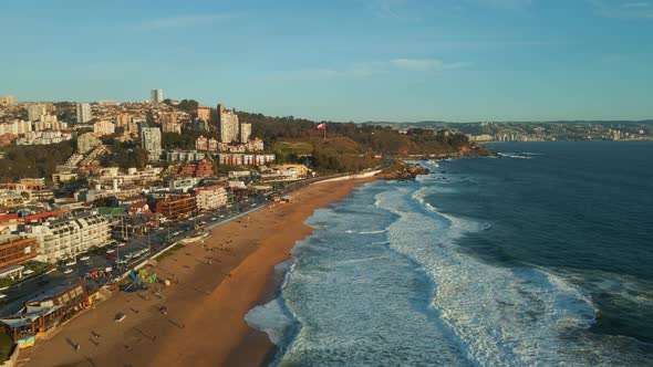 Aerial view flying down Reñaca golden sand waterfront with sunny scenic tourism retreat beach citysc