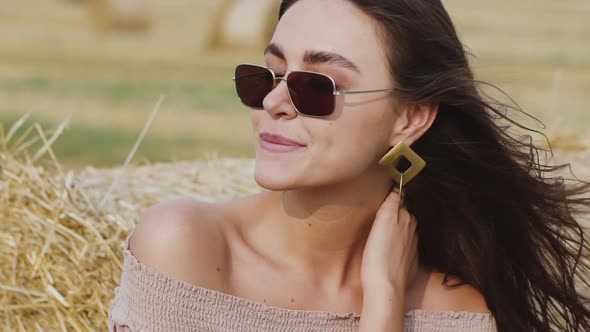 Portrait of Happy Woman in Sunglasses with Blowing Hair Smiling at Haystack