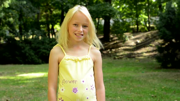 Little Happy Girl Stands in the Park and Smiles