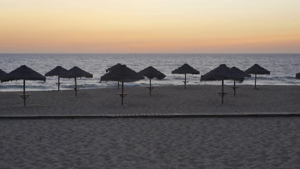 Empty beach at sunset in Comporta, Portugal with straw summer umbrellas