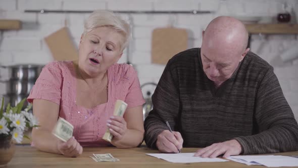 Close-up of Senior Caucasian Husband and Wife Settling Their Finances. Woman Holding Cash, Man