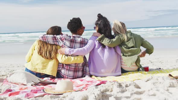 Happy group of diverse female friends having fun, sitting on blankets, embracing at the beach