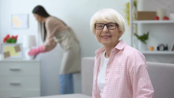 Smiling Aged Woman Looking at Camera, Housekeeper Wiping Dust in Room, Cleaning