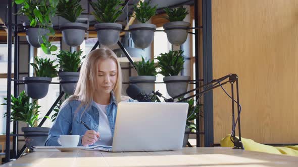 Female Blogger Sitting at Cafe with Laptop and Microphone