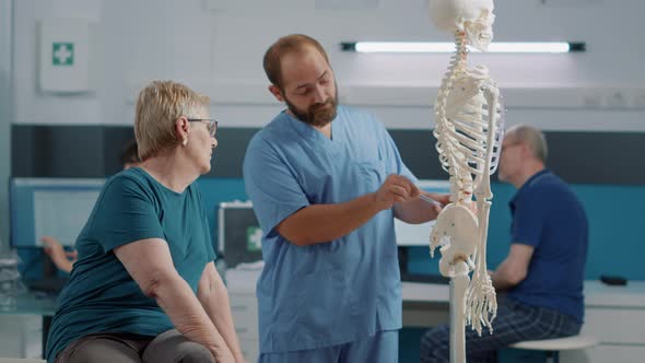 Male Osteopath Explaining Back Pain on Human Skeleton Bones