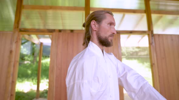 A Long-haired Caucasian Man in Light and Loose Clothing Practices Qigong Tai Chi in a Wooden