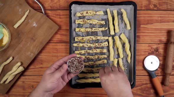 Sprinkling sesame seeds on top of sweet baked dough sticks.