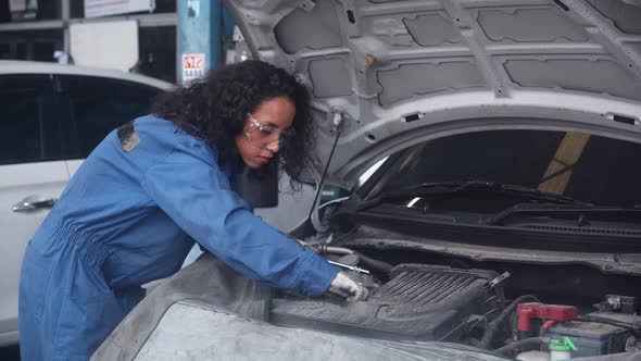 Young woman is mechanic repairing engine of car in the garage.