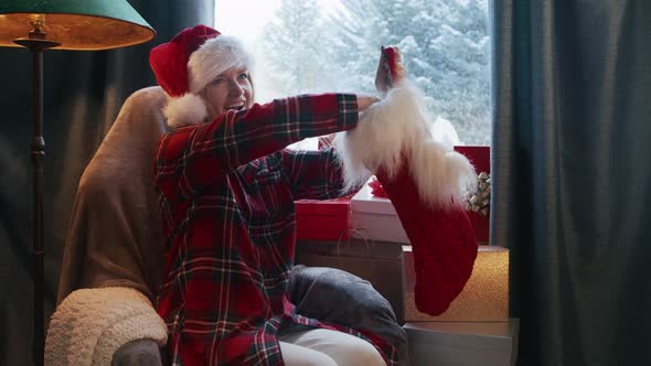 Happy Woman in Santa Hat Pulling Gift From Stocking Stuffer at Winter Blizzard