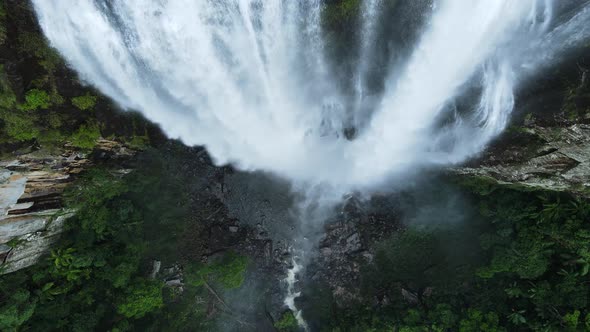 Unique camera angle of rushing water down a tropical mountain face into a lush rainforest rock pool.