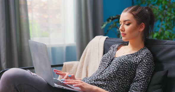 Smiling Millennial Girl Sit Relax on Couch Using Modern Laptop Browsing Unlimited Wireless Internet