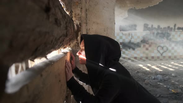 woman looks through gap in boarded up window in abandoned building