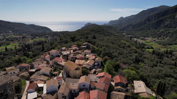 Forward droneshot over isolated village on top of green mountain in Greece. Blue sky with few clouds