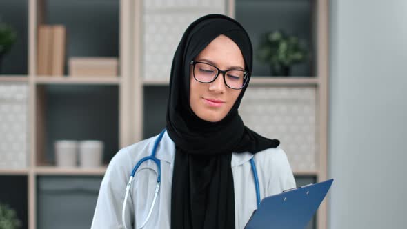 Portrait of Muslim Woman Doctor in Hijab Posing with Stethoscope Holding Folder Document at Clinic