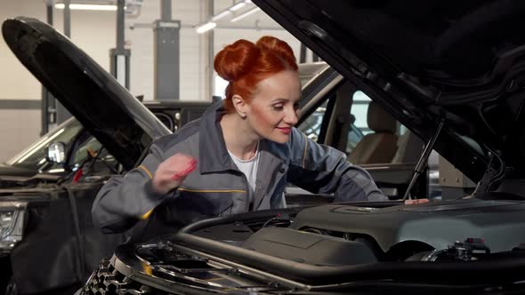 Attractive Female Car Mechanic Examining Automobile with an Open Hood