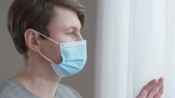 Closeup Face of Depressed Isolated Caucasian Man in Coronavirus Face Mask Looking Out the Window