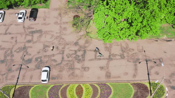 Two Cyclists Drive Through a Car Park Near the Park on a Spring Day