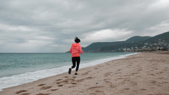 Woman is running on sand beach along stormy sea