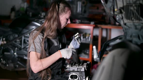 young woman repairing part of motorcycle engine in garage