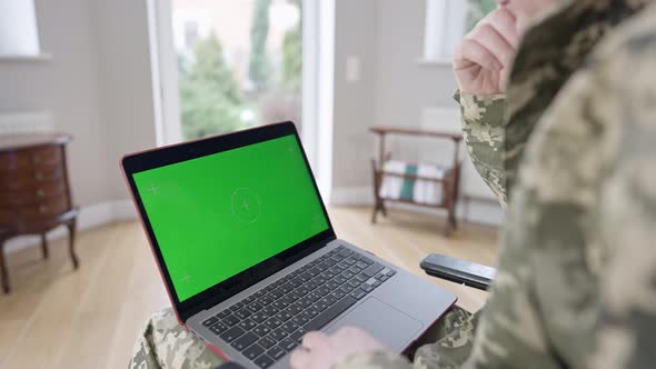 Laptop with Green Screen on Knees of Unrecognizable Caucasian Military Man Indoors