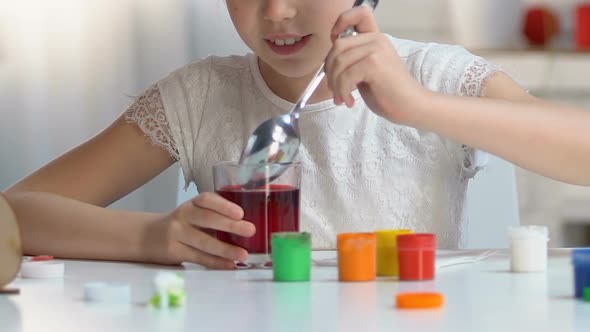 Excited Girl Taking Colored Egg From Glass With Red Food Coloring