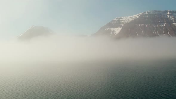 Drone Flight Towards Misty Mountains With Snow Over Fjord