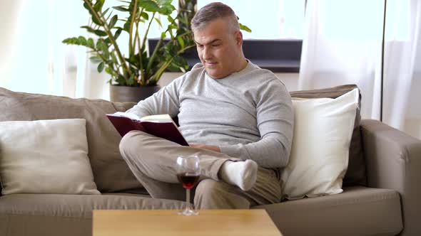 Happy Man Drinking Wine and Reading Book at Home 