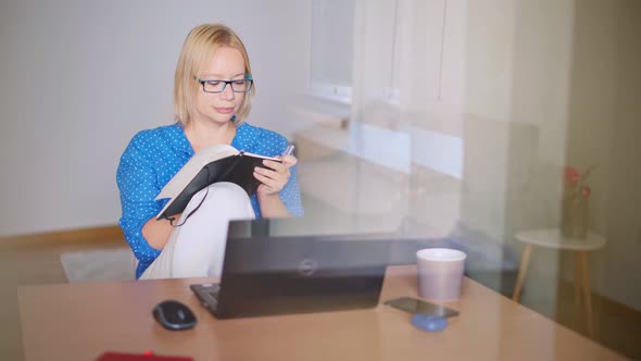 Adult Blond Woman Making Notes in Her Notebook While Watching a Webinar