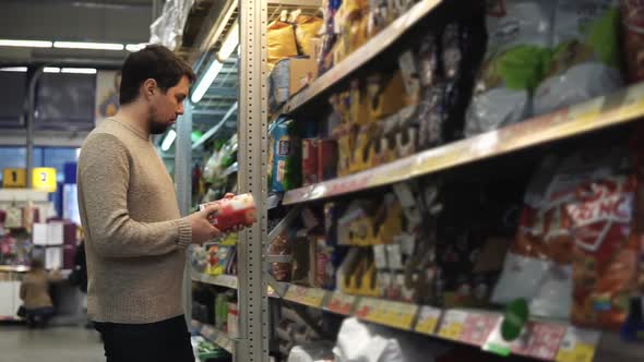 Adult Man Examines Box of Potato Chips but Then Puts It Back